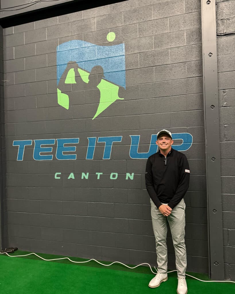 Maxwell Moldovan stands in front of the Tee It Up Canton logo